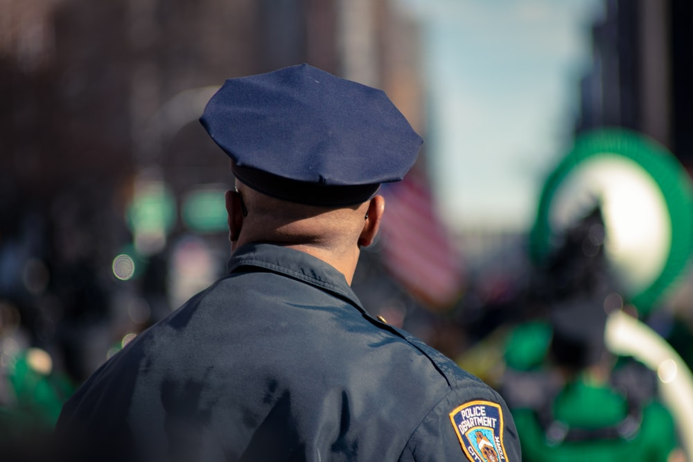 A Uniformed Police Officer Standing With His Back Facing The Camera