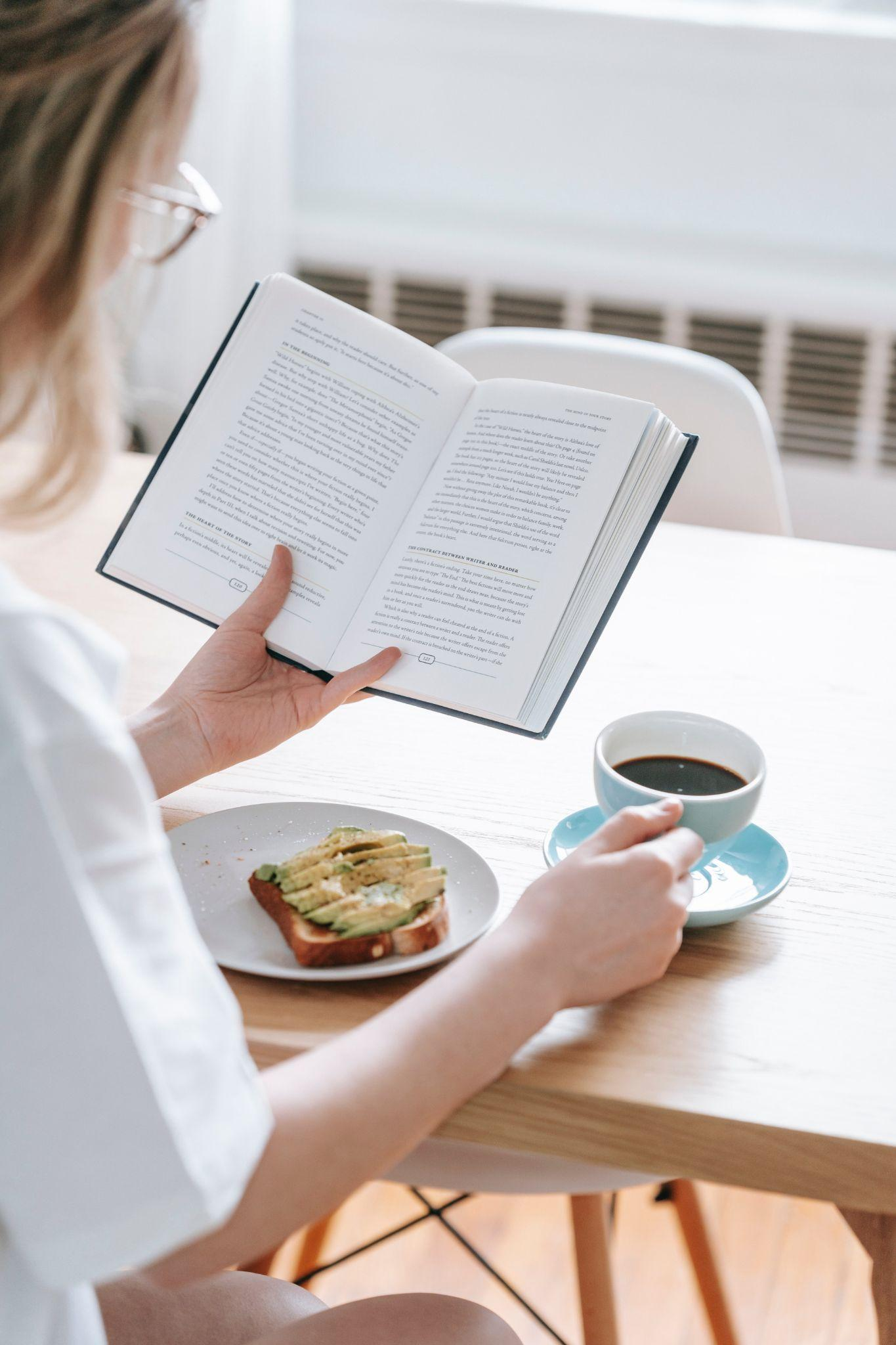 A woman reading a book while having breakfast