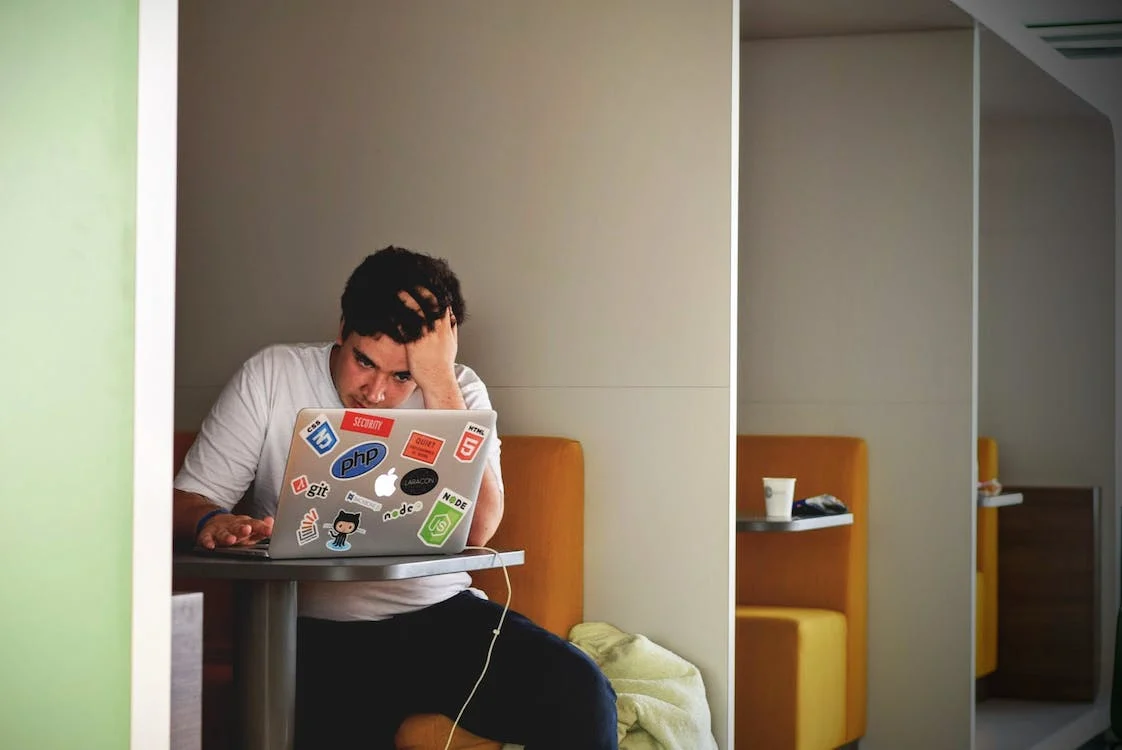 An image of a man looking anxious while working on a laptop