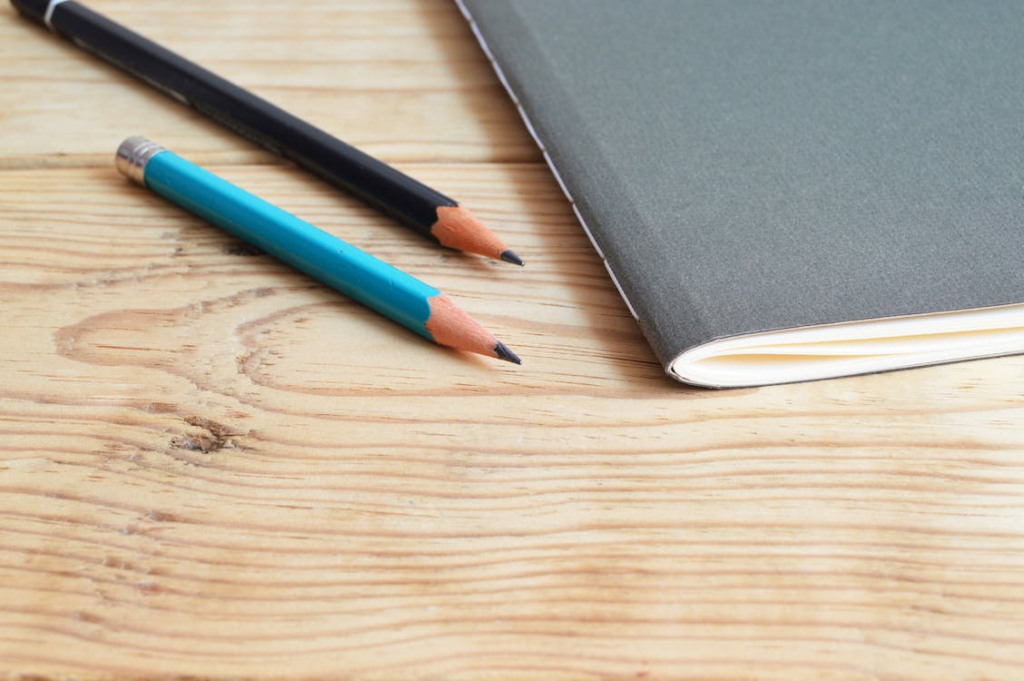 An image of a notebook and pencils placed on a wooden desk