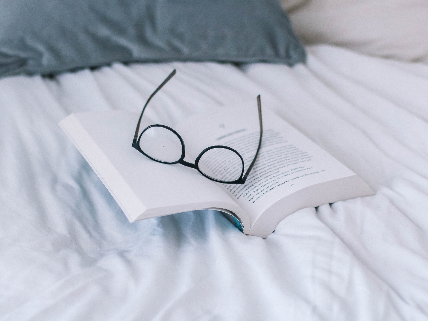 a book and a pair of glasses on a bed
