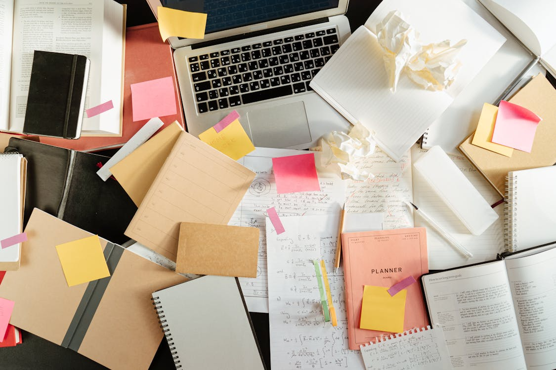Crumpled papers, books, and notes next to a laptop