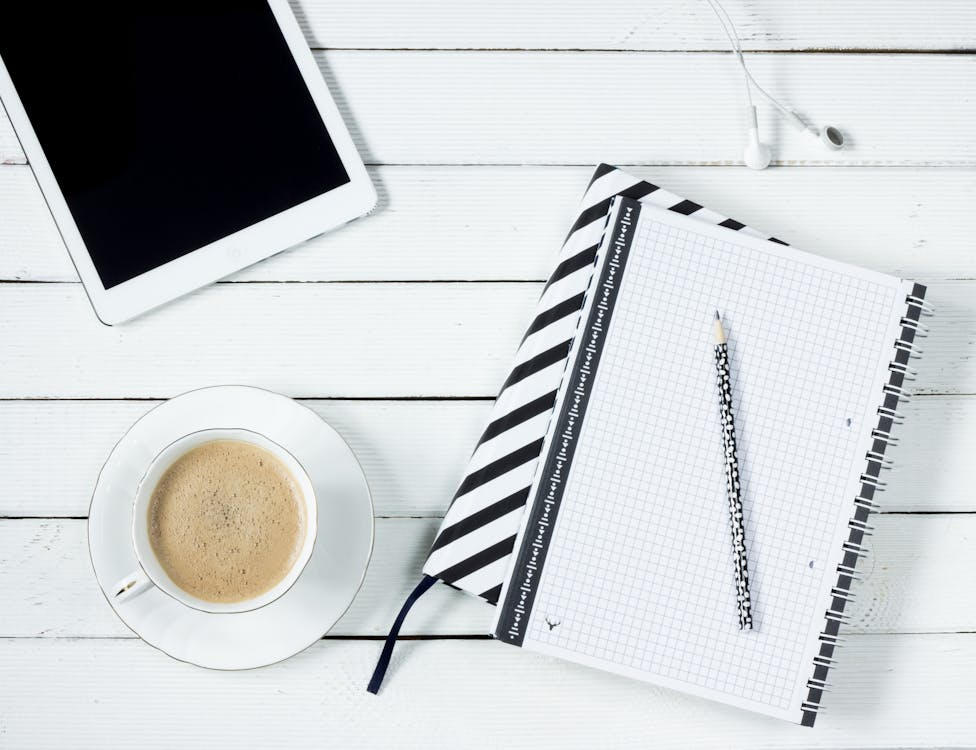 A tablet and a cup of coffee beside a notebook